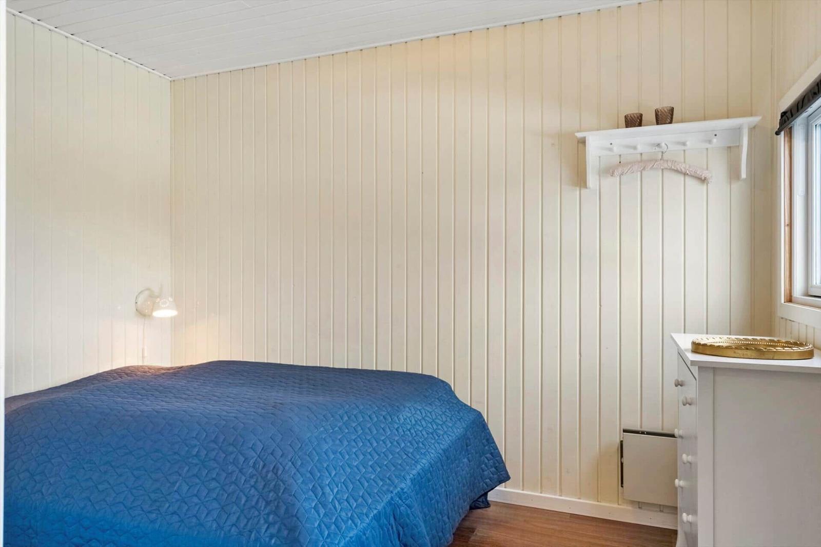 Schlafzimmer mit Bett, Schrank und Wandlampe. Holzwandverkleidung und Fenster.