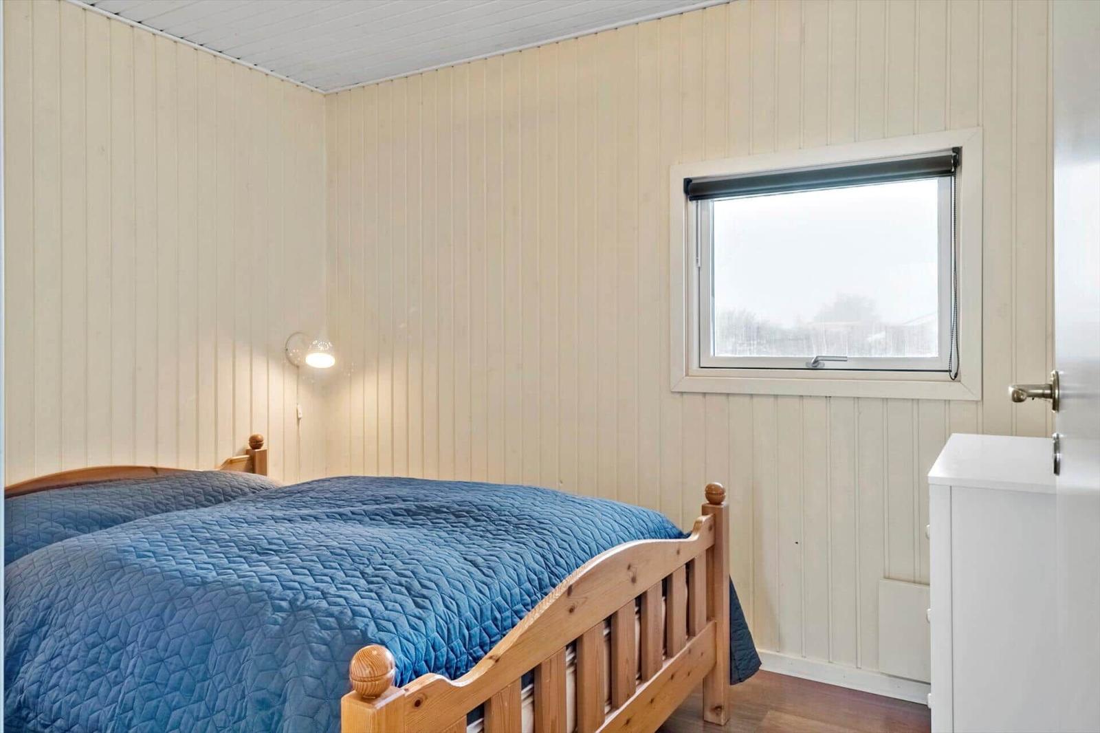 Schlafzimmer mit Holzbett, blauer Bettdecke und Fenster mit Rollladen.
