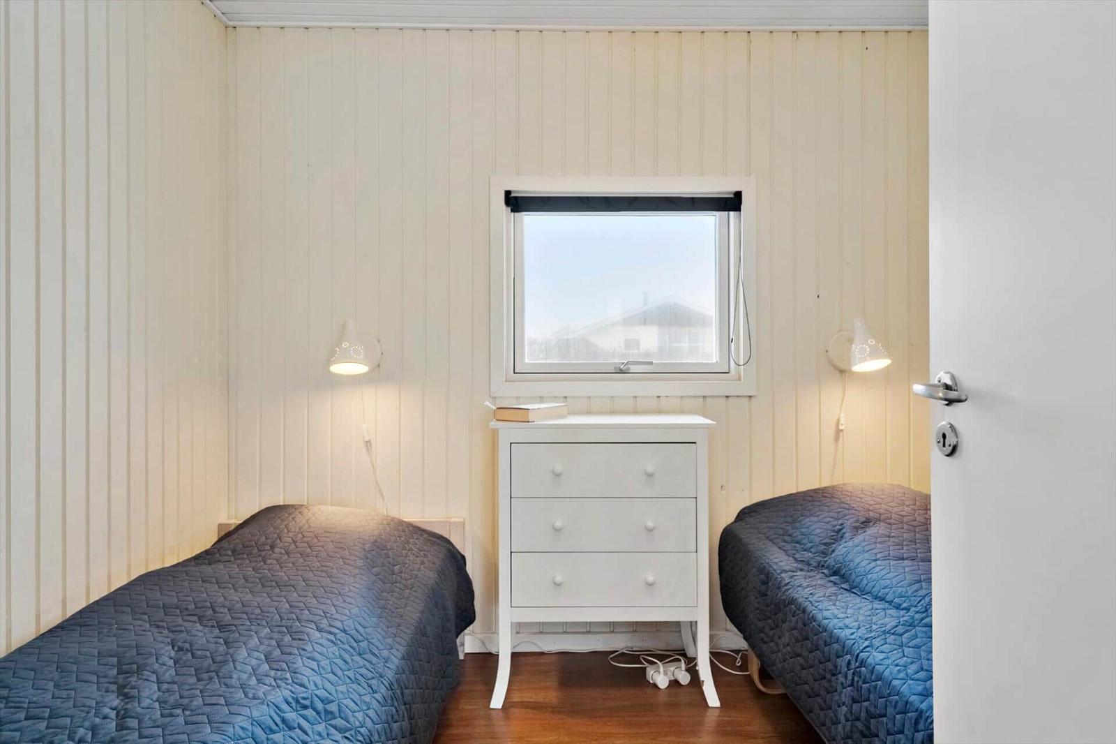 Zwei Betten mit blauen Bezügen stehen in einem Raum mit Holzwand und Fenster.