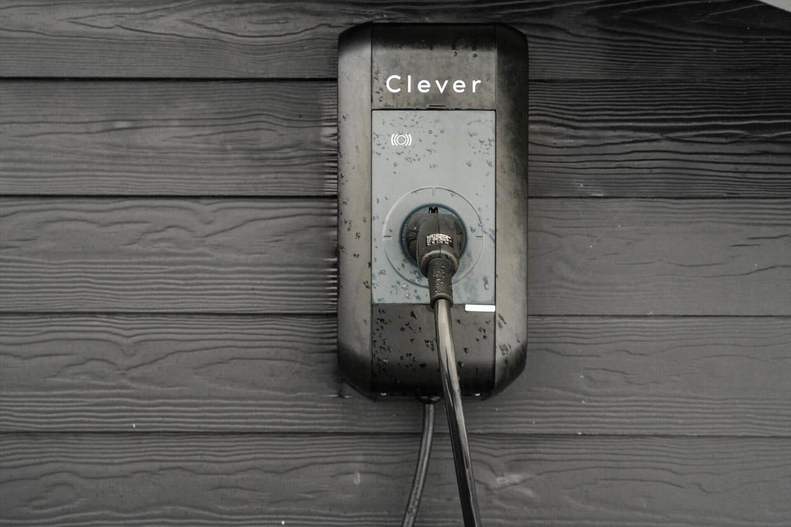 Außenliegender Elektroauto-Ladepunkt an dunkler Holzwand mit eingestecktem Kabel.