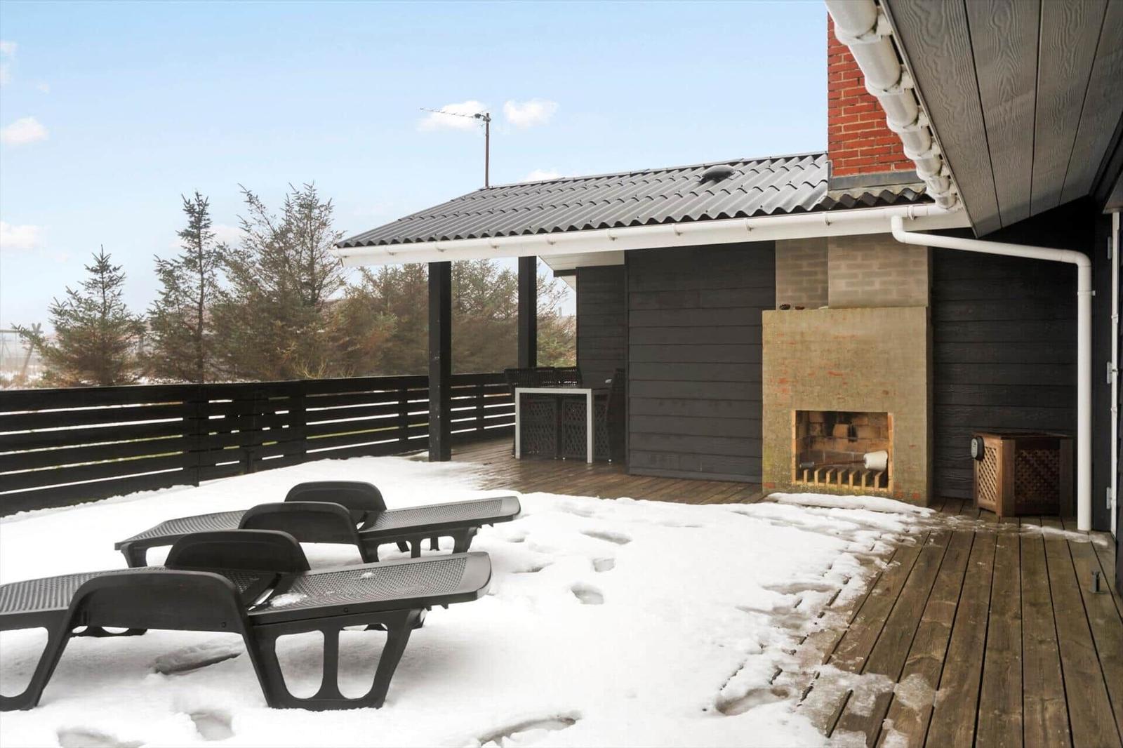 Terrasse mit Schnee, Liegen und Außenkamin. Holzdecke und schwarze Holzwände.