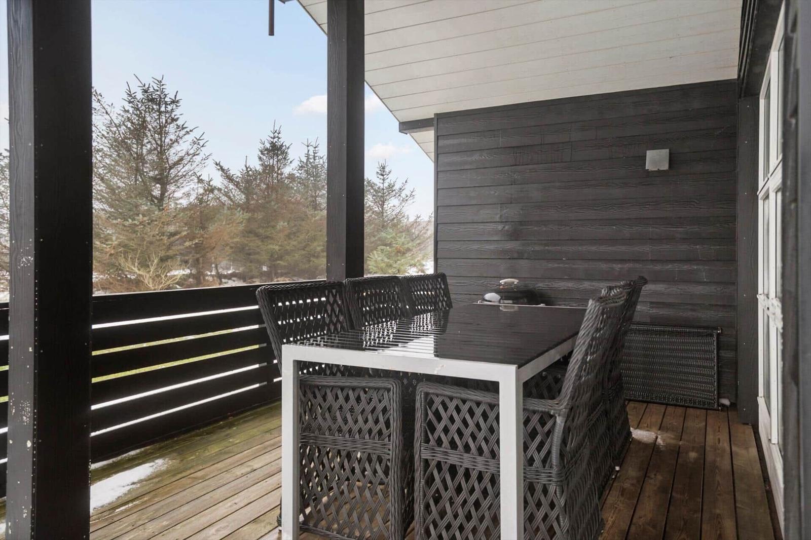 Terrasse mit Tisch und Stühlen, Blick auf Wald und Himmel.