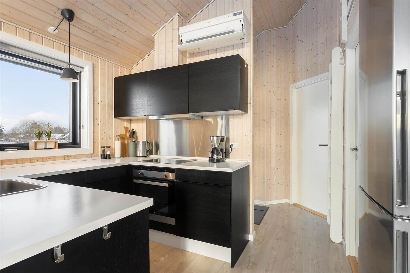 Modern kitchen with black cabinets, stainless steel appliances, and wood paneling.