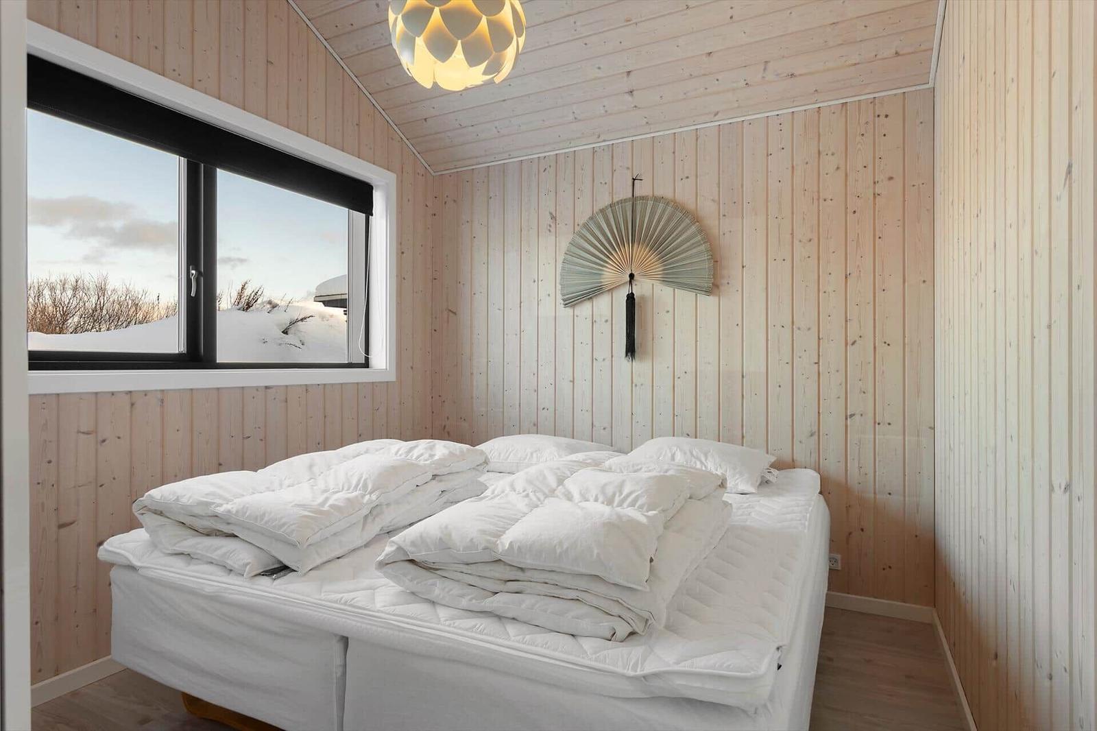 Bedroom with wooden walls, large window, and white bed.