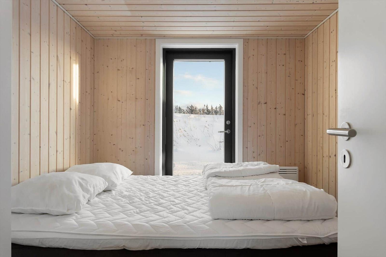 Bedroom with wooden walls and bed. Through door view of snowy landscape.