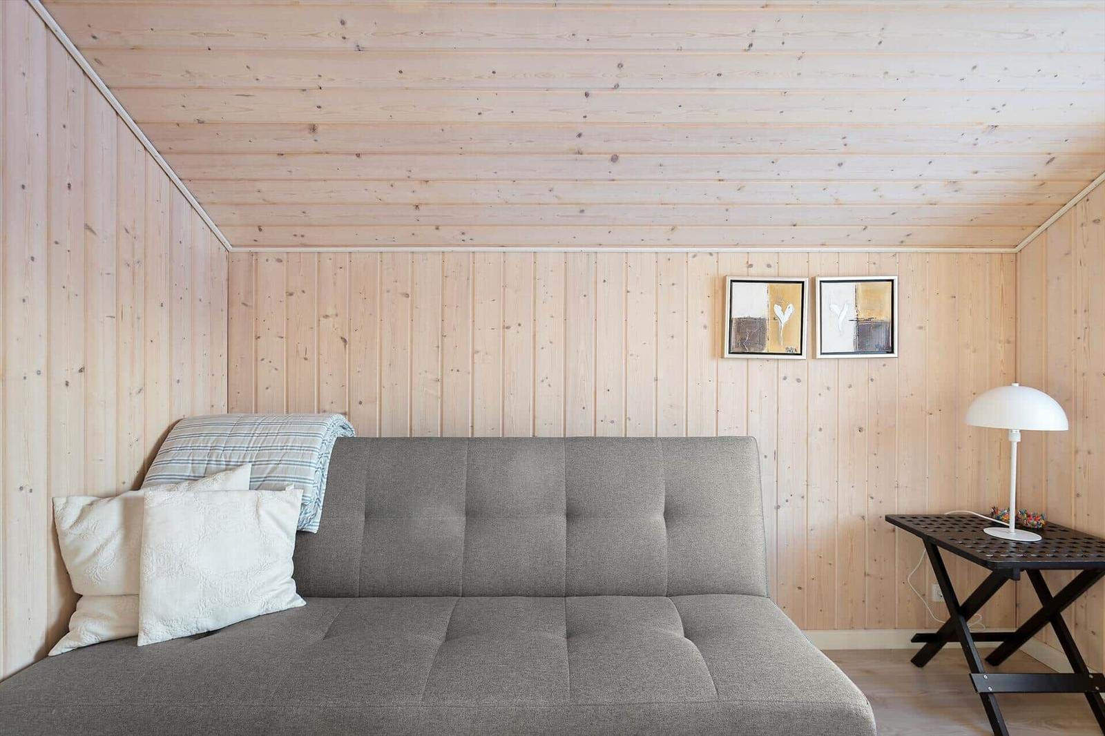A gray sofa with cushions and a blanket in a room with wooden walls and two pictures.