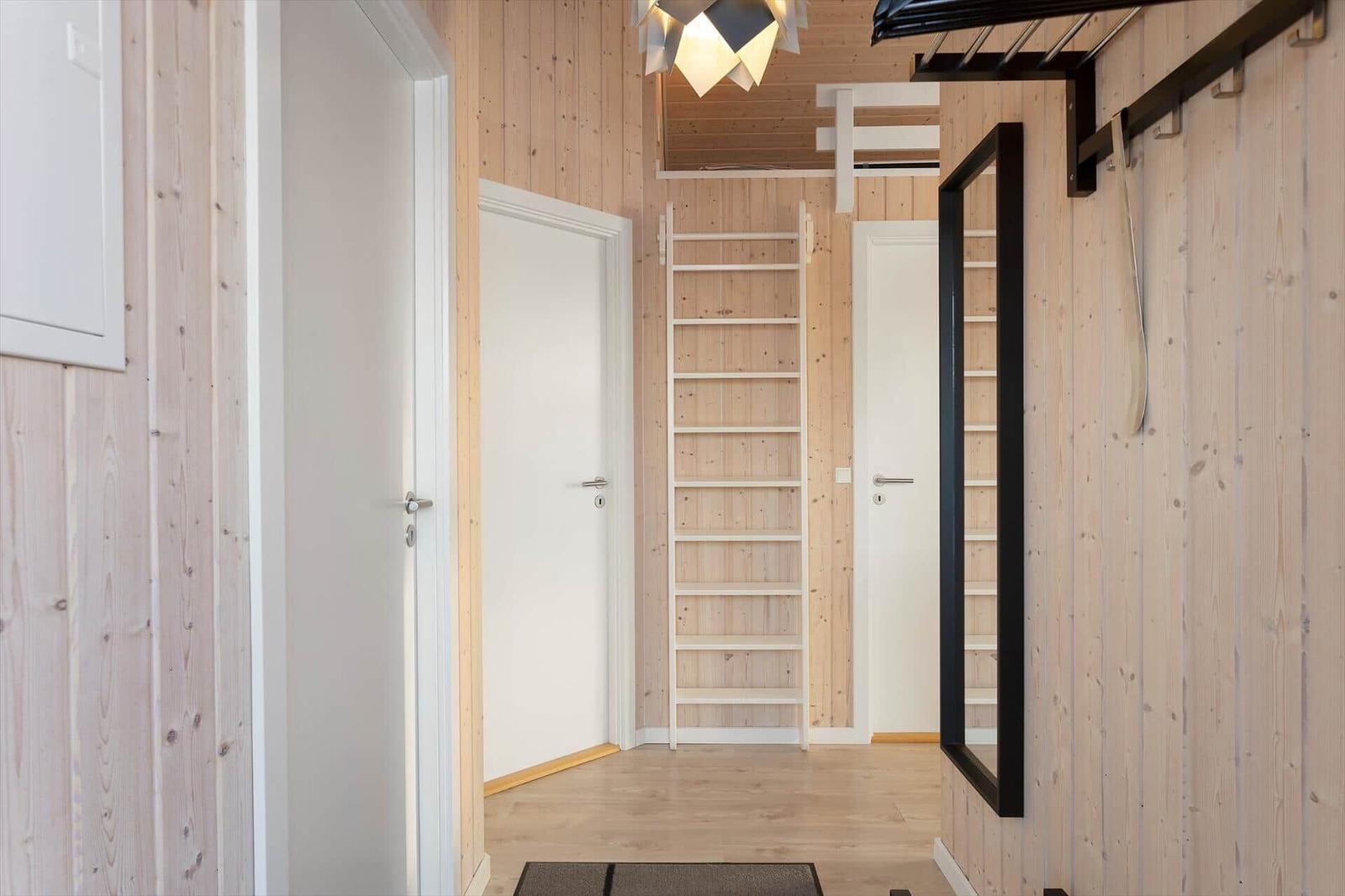 Hallway with wooden walls, ladder, and mirror. Doors and floor are light.
