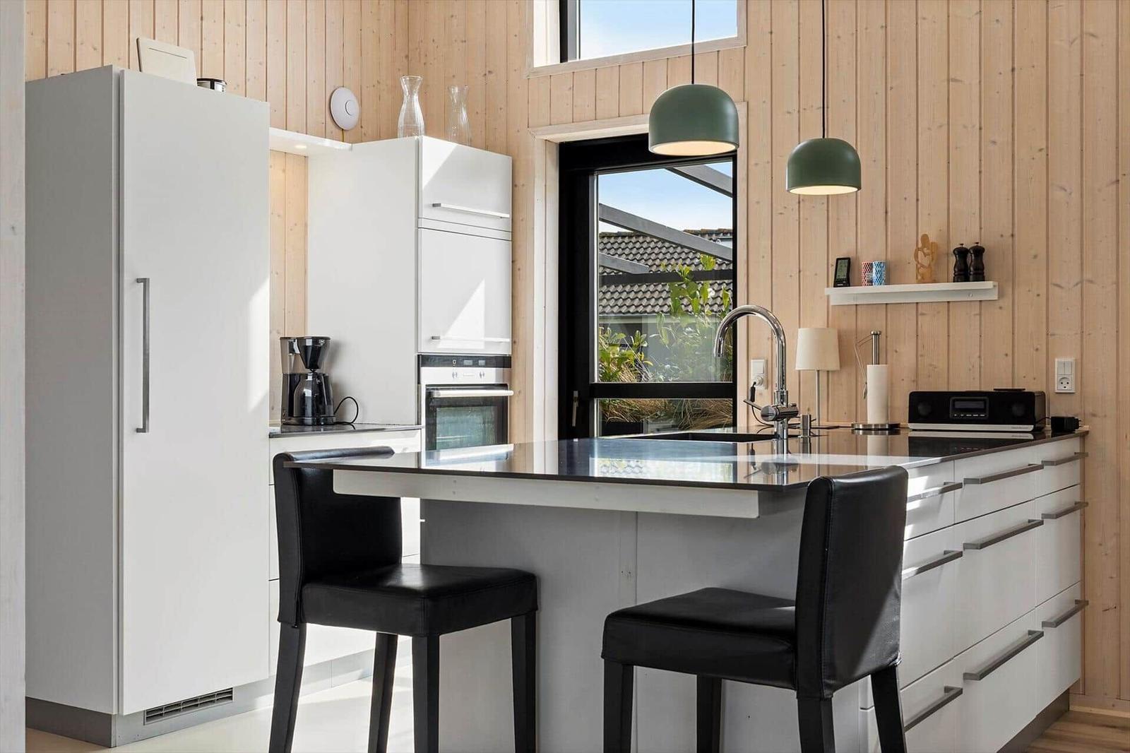 Moderne Küche mit weißen Schränken, schwarzen Barhockern und Holzwänden. Große Fenster mit Blick auf Garten.