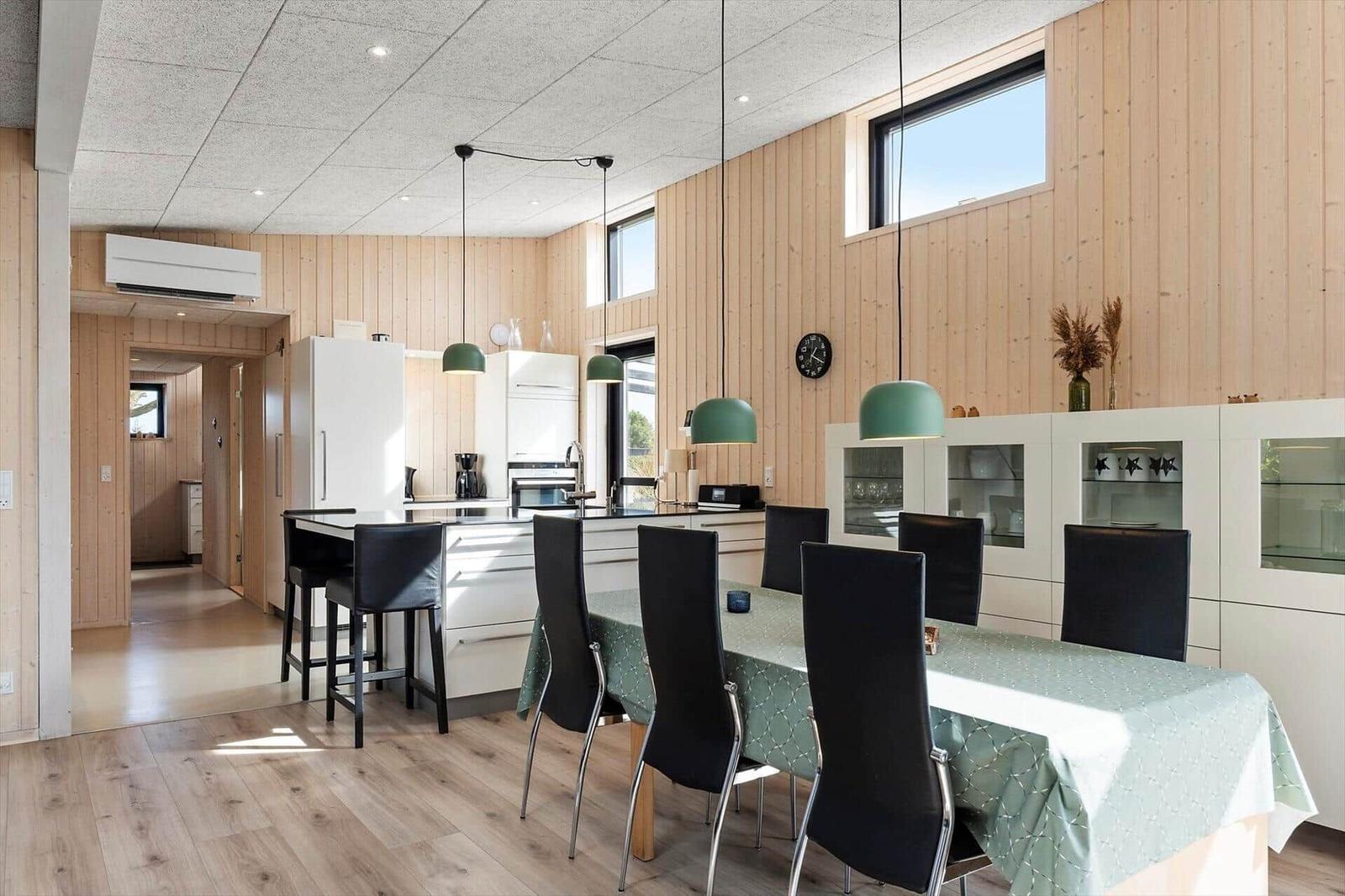 Moderne Küche mit Esstisch, schwarzen Stühlen und grünen Hängelampen an Holzwänden.