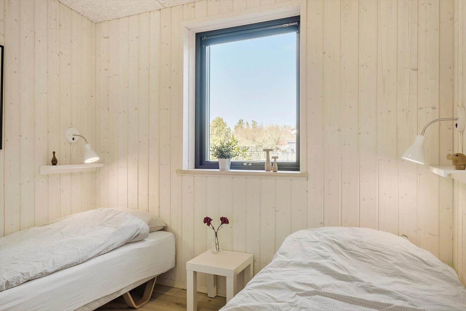 Zwei Betten mit weißen Bettwäsche, Holzwände und Fenster mit Blick auf Bäume.
