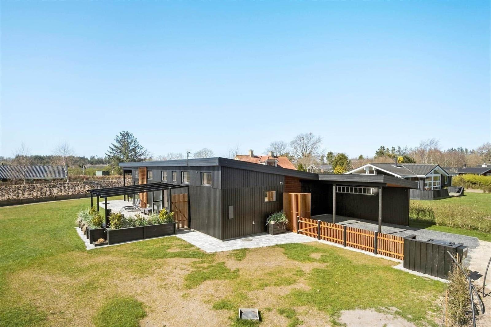 Moderne Villa mit Holzverkleidung, Garten und Terrasse unter klarem Himmel.