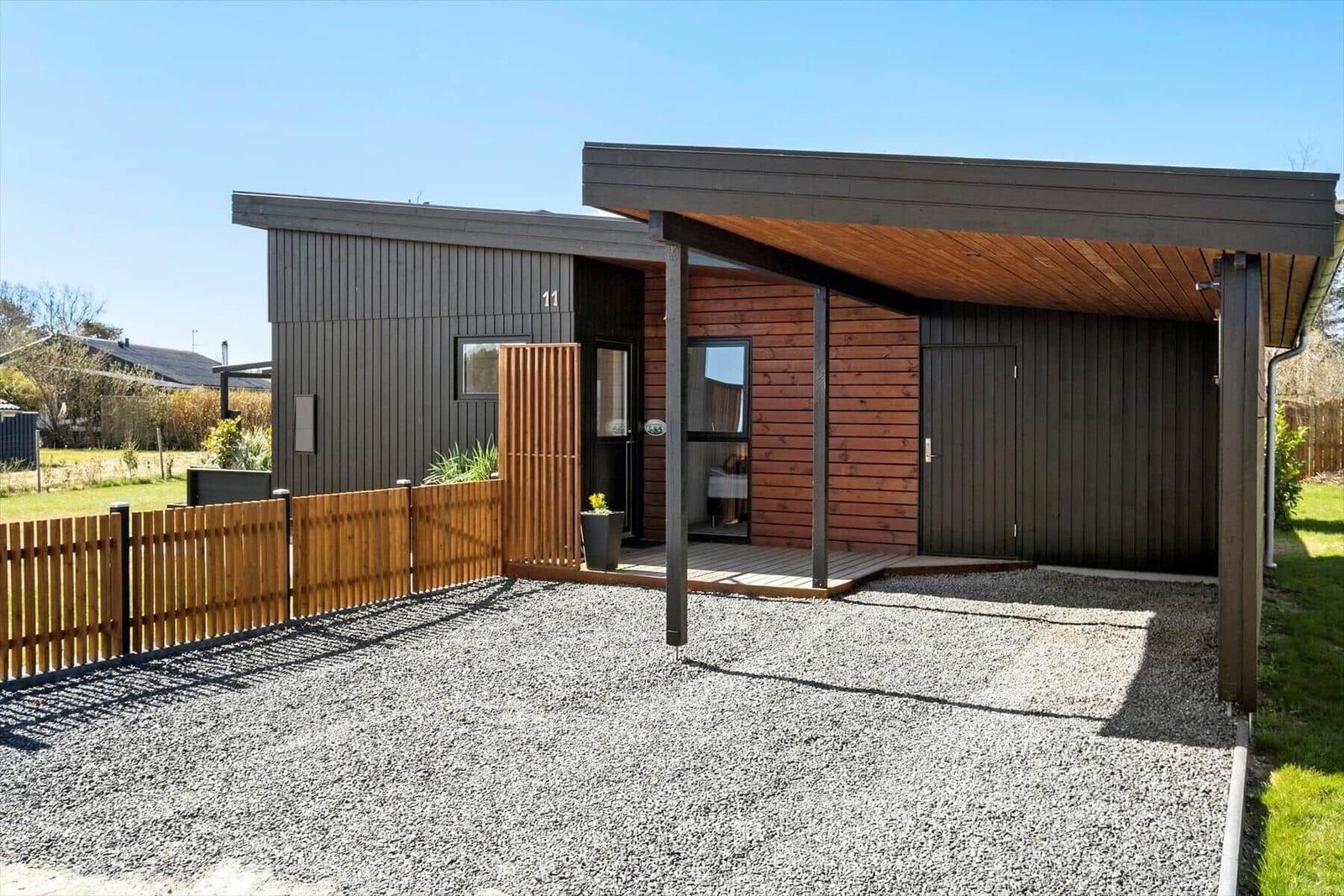 Moderne Hütte mit Holzverkleidung, überdachter Terrasse und Kiesplatz.