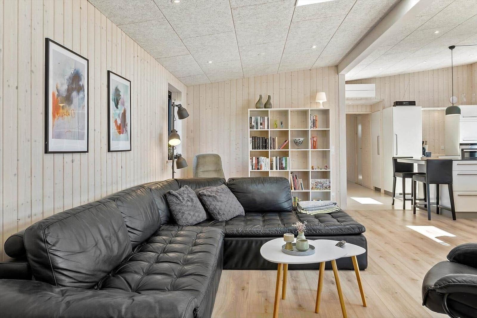 Wohnbereich mit Leder-Sofa, Bücherregal und Küchenbereich im Hintergrund.