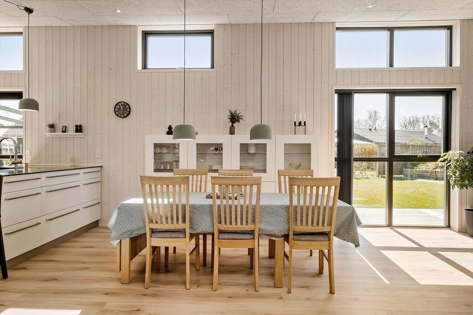 Esszimmer mit Holztisch, Stühlen und Glaswand. Küche und Terrasse sind sichtbar.