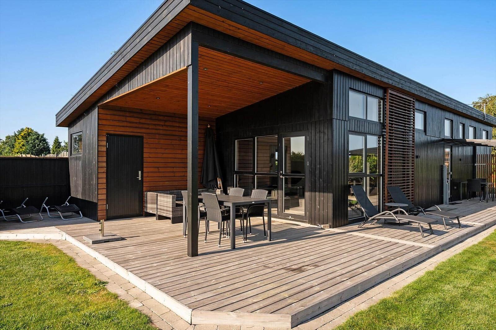 Moderne Holzhütte mit Terrasse, Gartenmöbeln und großem Fensterbereich.