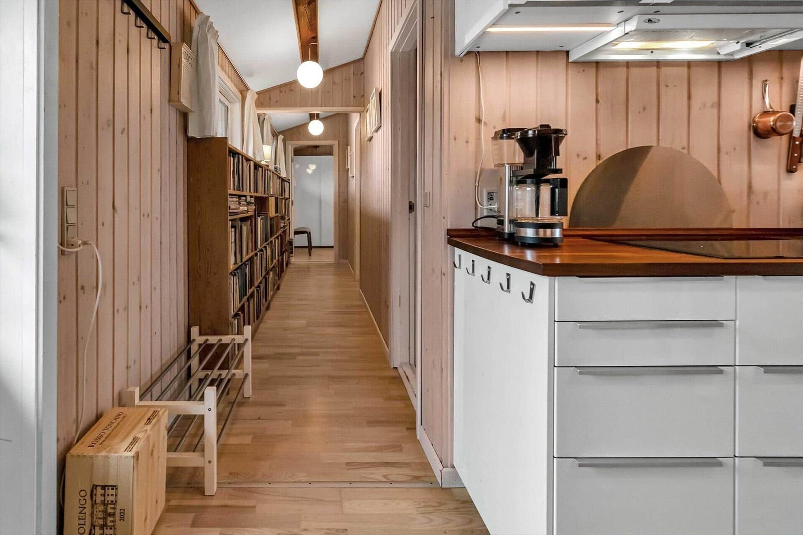 Küche mit Holzoberfläche und weißen Schränken. Flur mit Bücherregal und Holzwand.