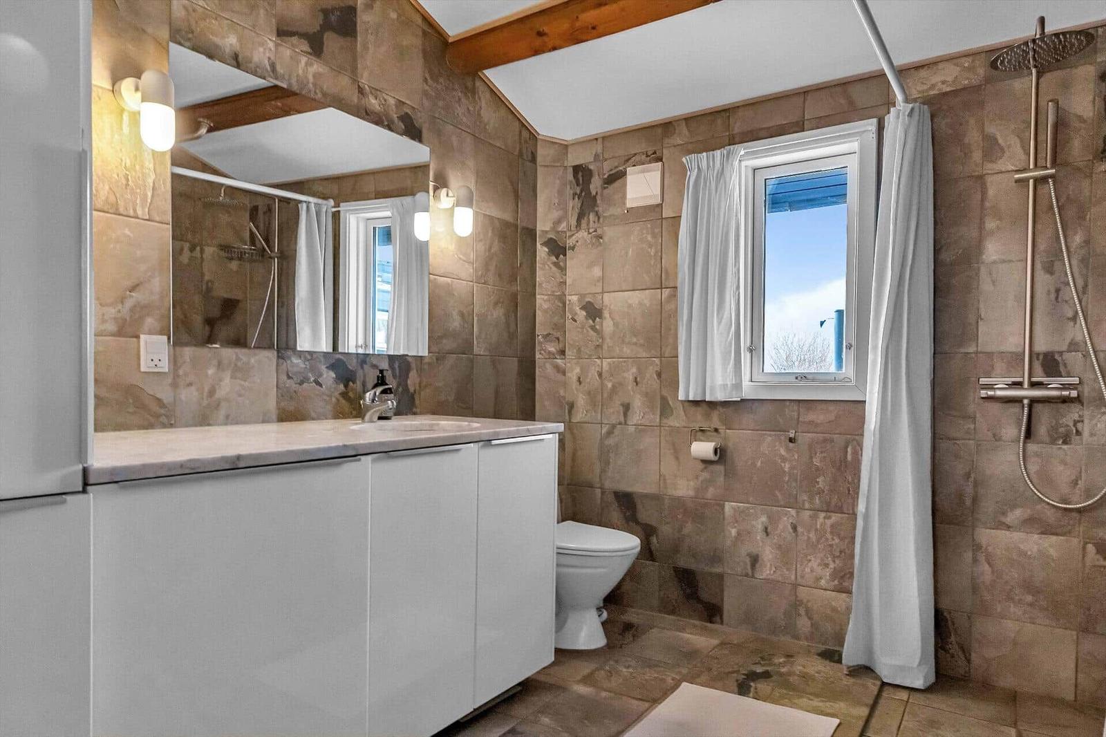 Badezimmer mit Dusche, Toilette und Waschbecken. Wände und Boden sind mit Steinplatten verkleidet.