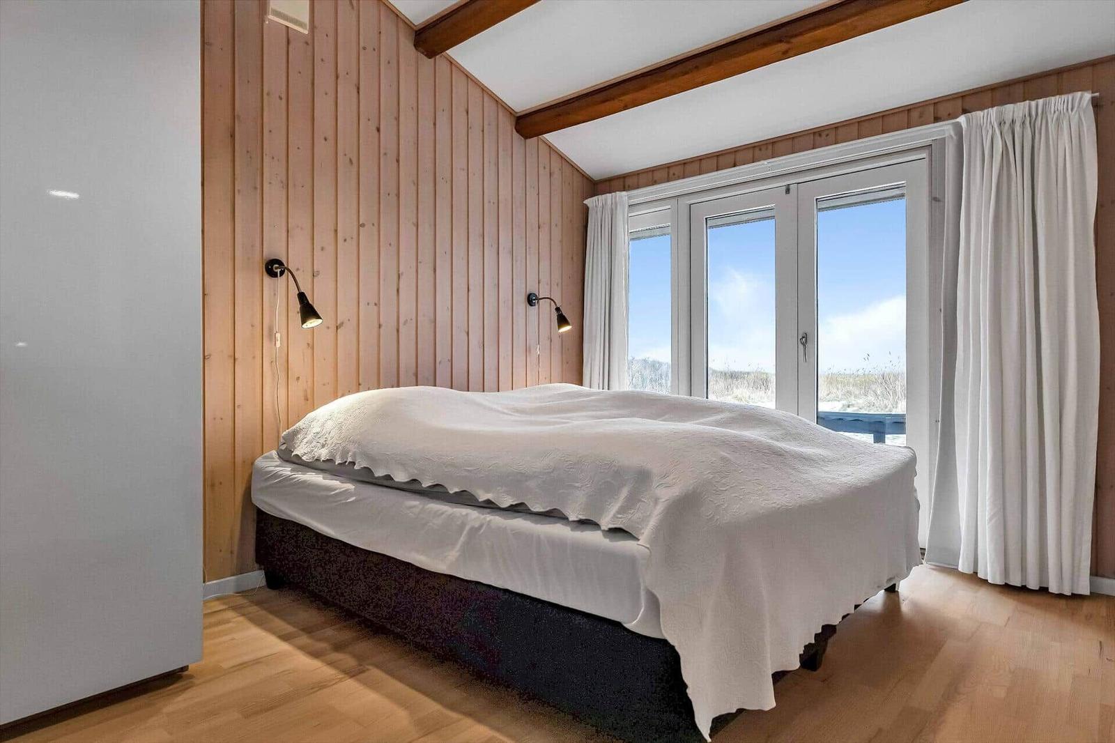 Schlafzimmer mit Bett, Holzwand und Fenster zur Aussicht.