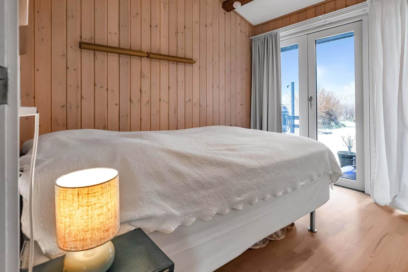 Schlafzimmer mit Bett, Holzwand und Fenster zur Aussicht.