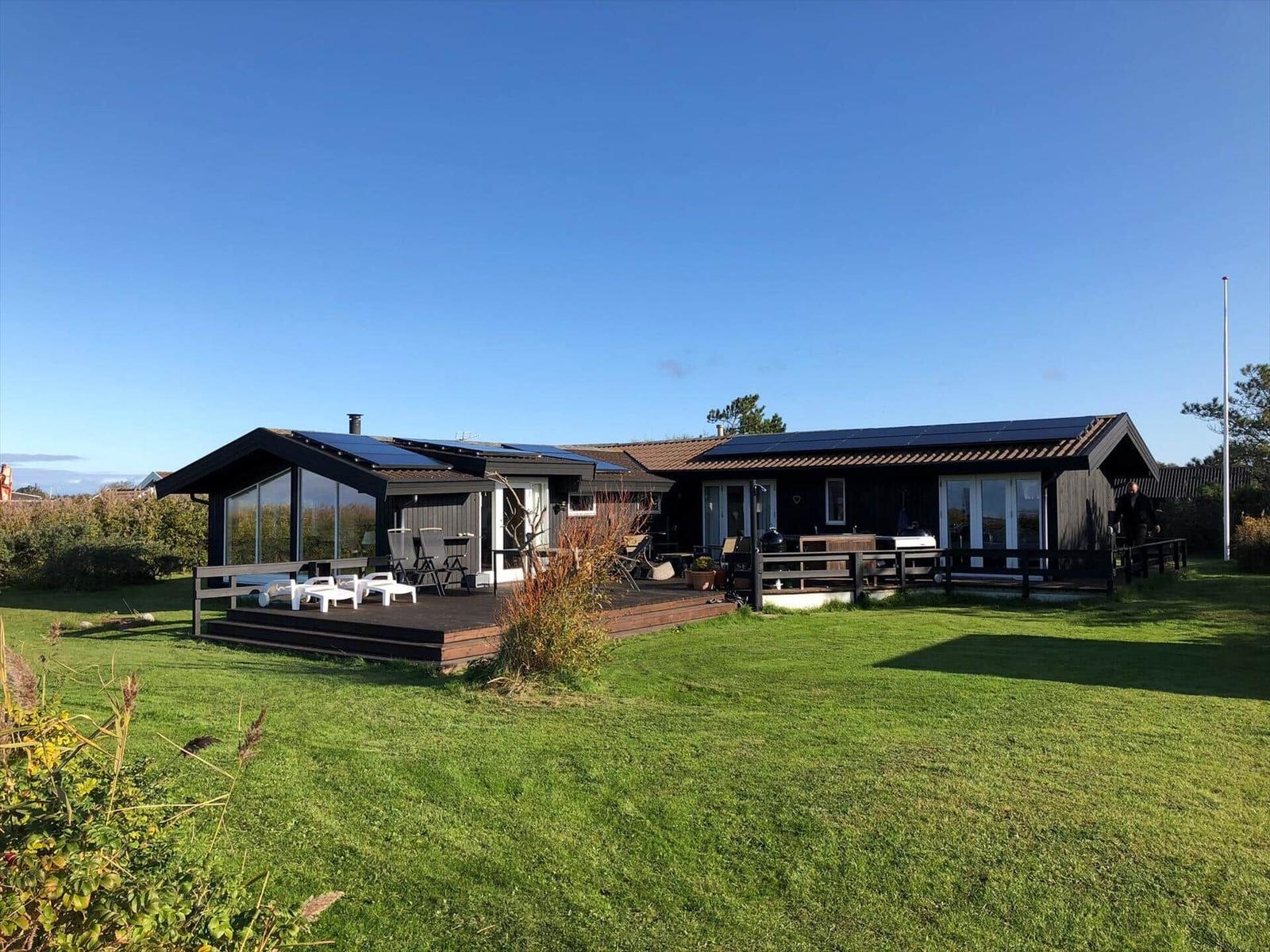 Moderne Ferienwohnung mit Terrasse, Garten und Solaranlage unter blauem Himmel.