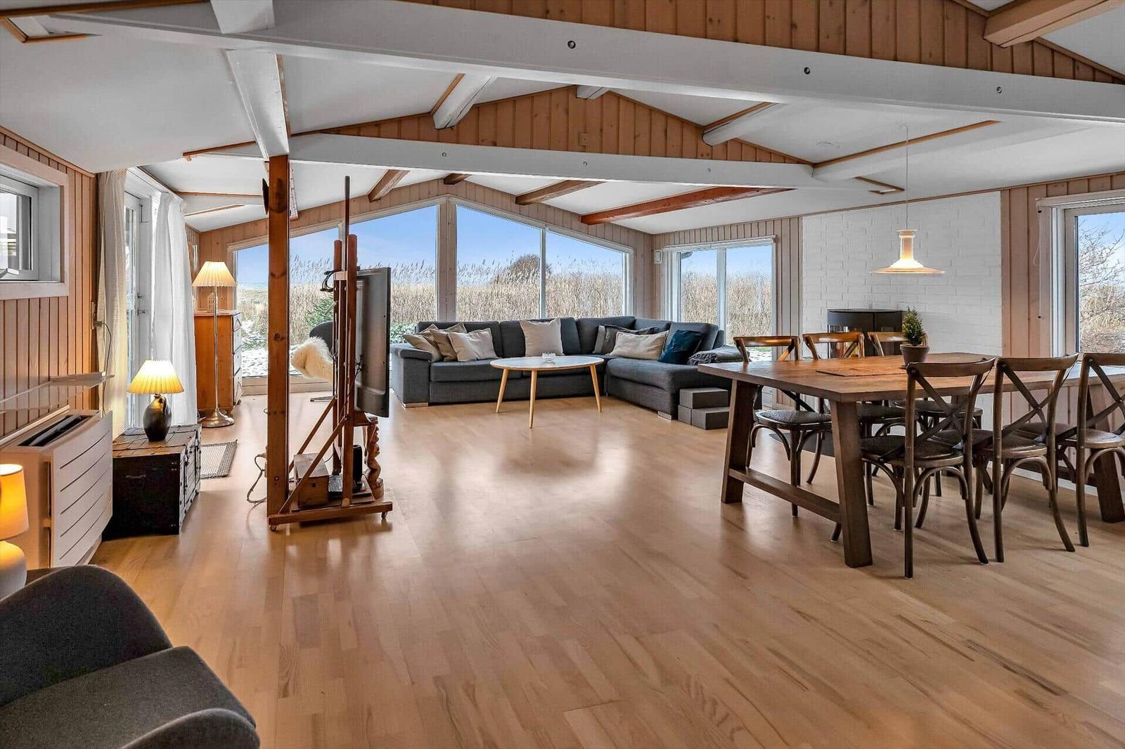 Großes Wohn- und Esszimmer mit Holzboden, Sofa und Esstisch. Große Fenster mit Blick auf die Landschaft.