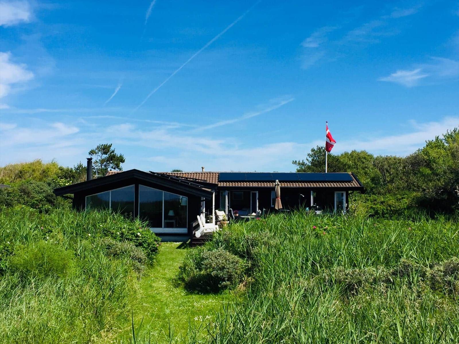 Ein Haus mit großem Fensterbereich, Terrasse und dänischer Flagge im Grünen.