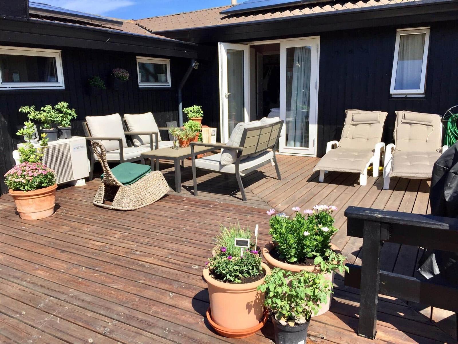Terrasse mit Sitzgelegenheiten und Pflanzen vor einem Haus mit Schiebetüren.