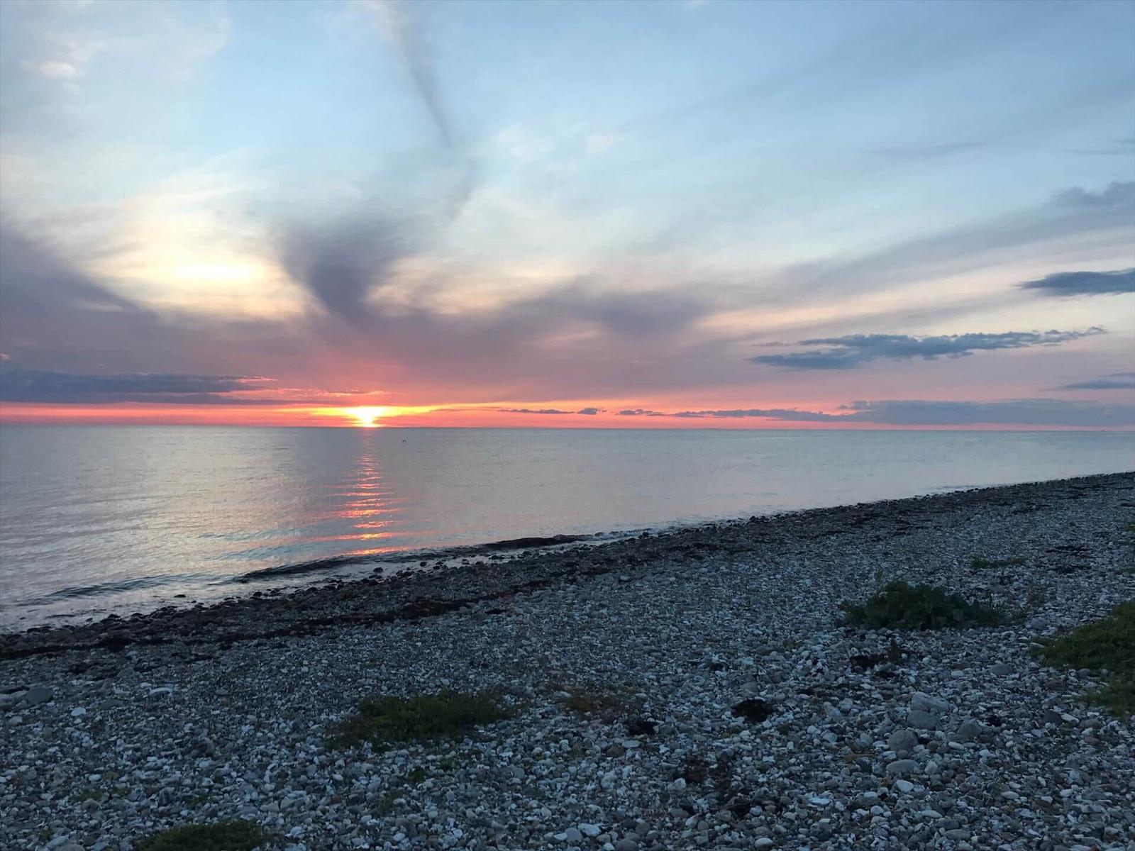 Sonnenuntergang über dem Meer mit Steinhügel im Vordergrund.