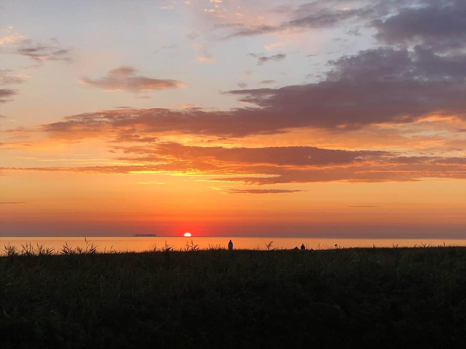 Sonnenuntergang über dem Meer mit Silhouetten von Menschen und einem Schiff im Hintergrund.