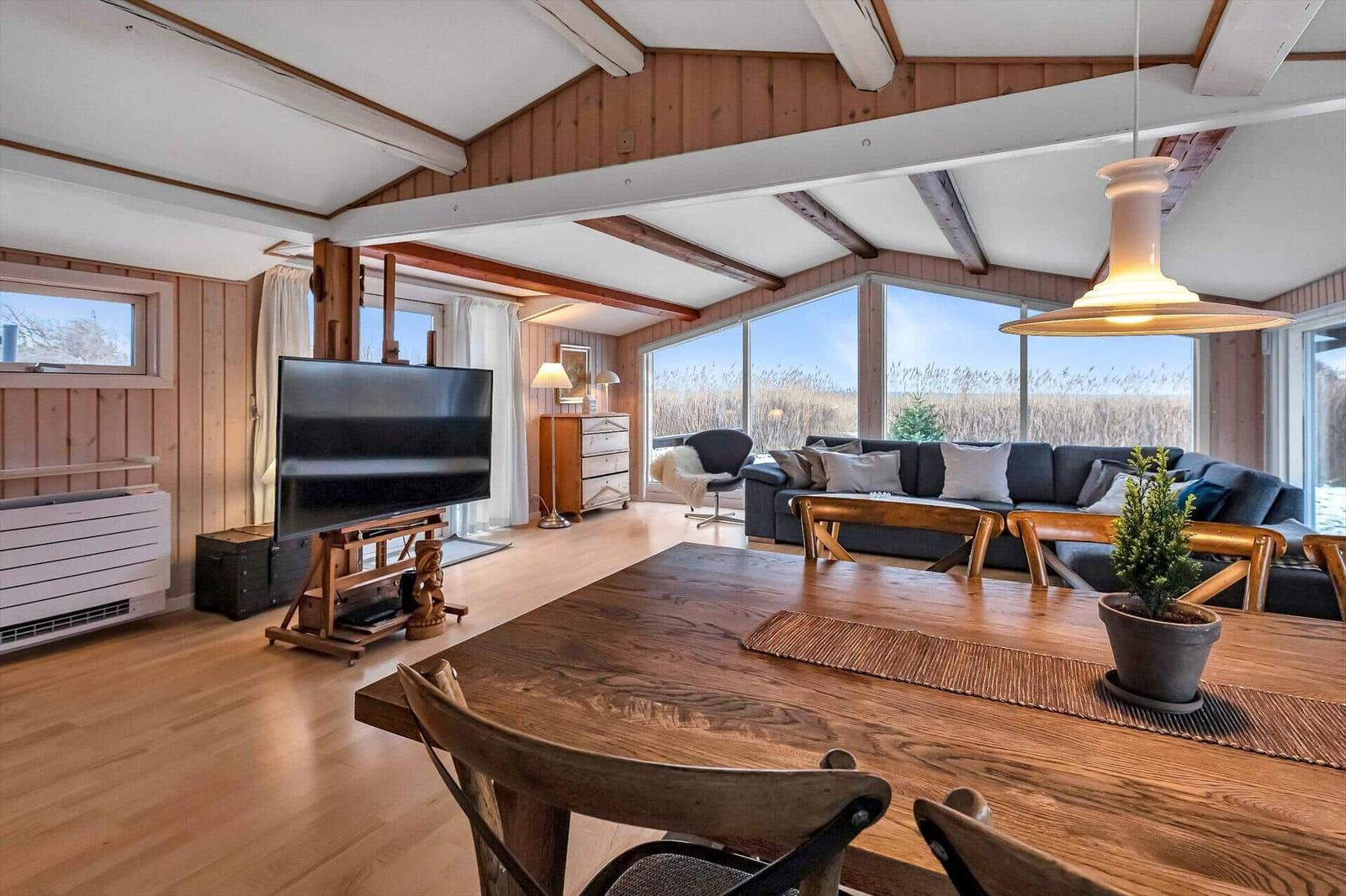 Großer Wohn- und Essbereich mit Holzdecke, TV und großem Fenster zur Aussicht.