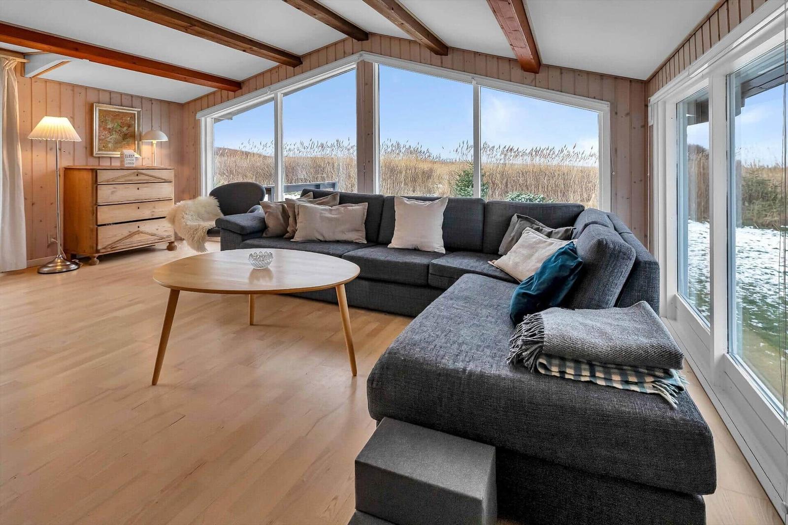 Wohnzimmer mit großem Sofa, Holzboden und Blick aufs Wasser und Gras.