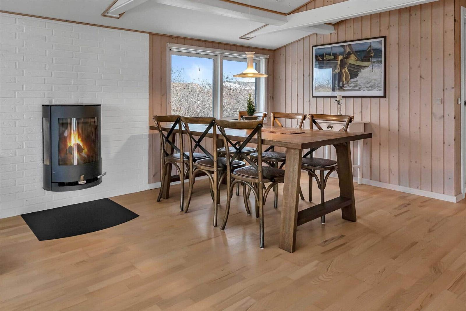 Esszimmer mit Holztisch, Stühlen und Kamin. Holzwände und Fenster mit Blick.