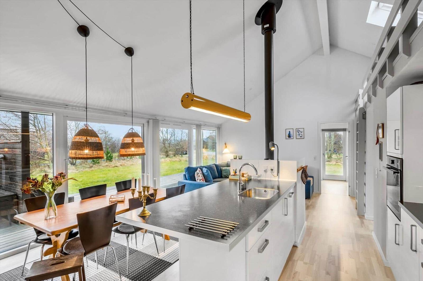 Kitchen with dining area and garden view. Wooden floor, white cabinets, and black countertop.