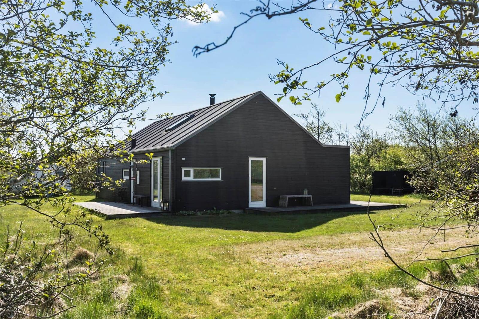 Modern dark-clad cabin with white windows and terrace in the green.