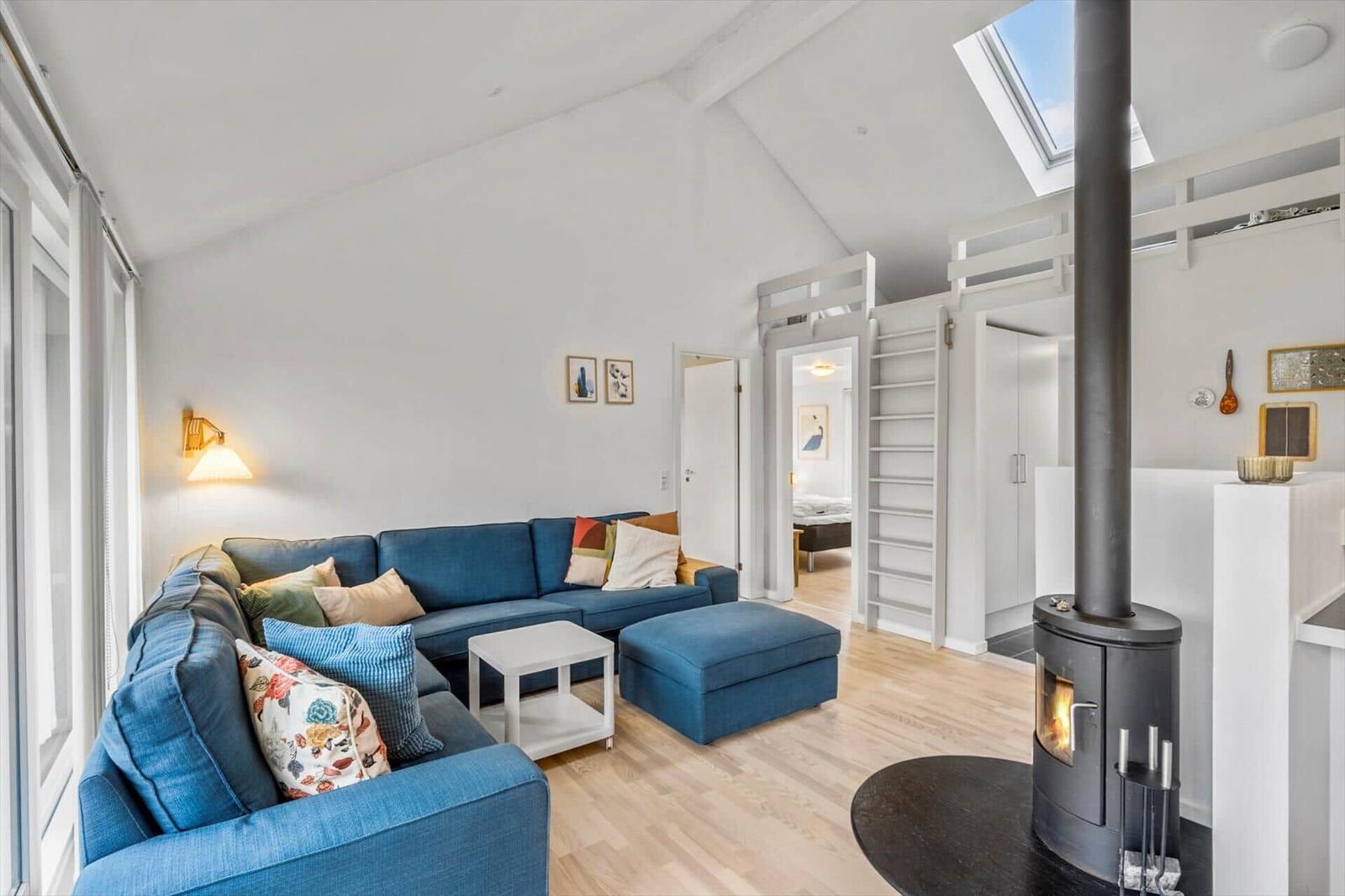 Living room with blue sofa, fireplace, and sloped ceiling. Stairs lead to upper level.