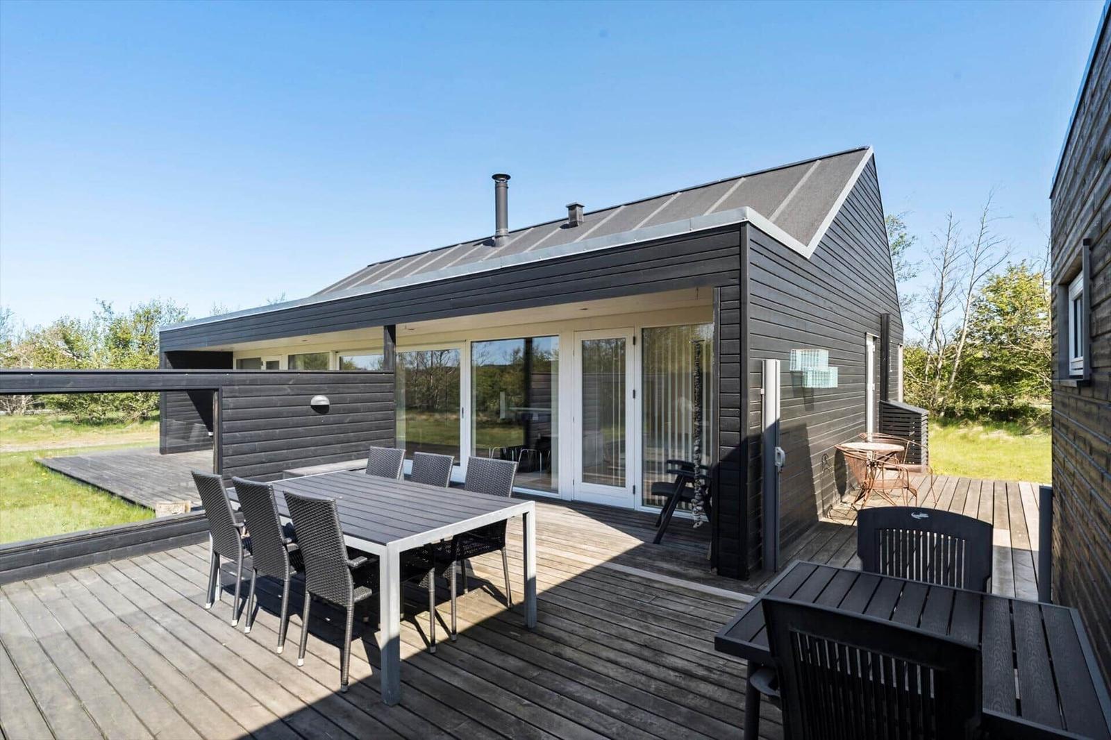 Modern villa with terrace, seating, and garden. Glass doors lead inside.