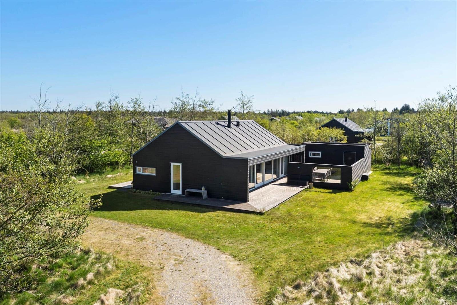 Modern wooden cabin with terrace and garden in green surroundings.