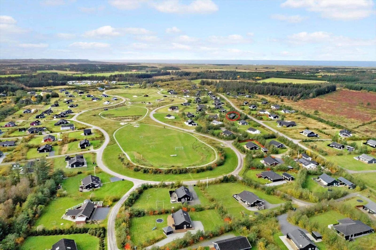 Aerial view of a residential area with houses, green lawns, and winding paths near the sea.