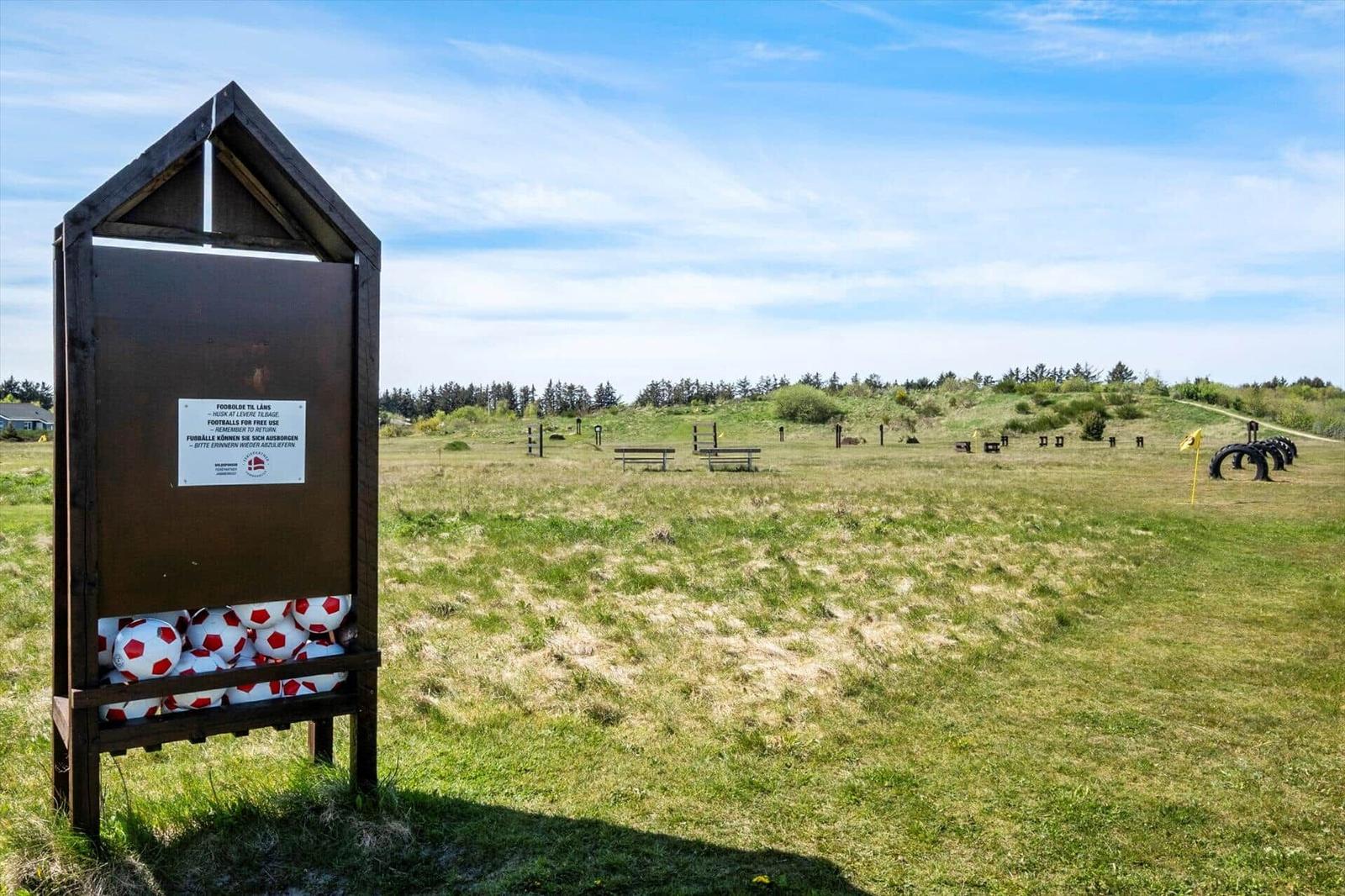 Football box with balls in a grass field. Benches and obstacles are visible in the background.