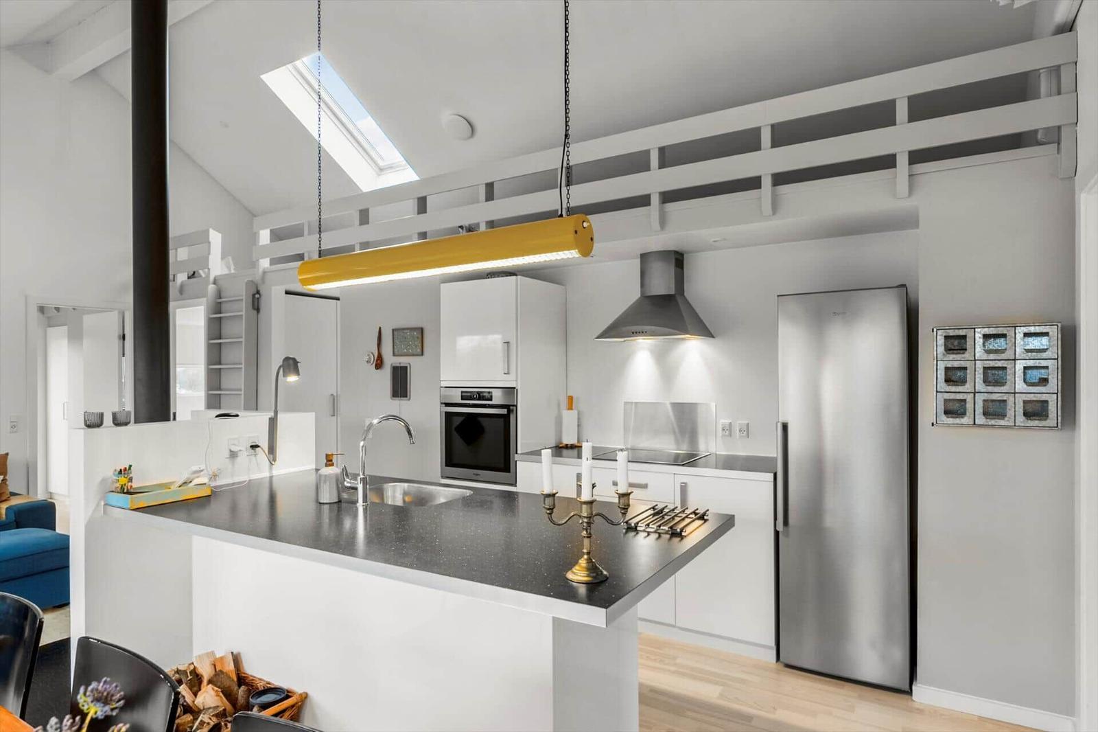 Modern kitchen with stainless steel appliances, dark countertop, and yellow pendant light under sloped ceilings.