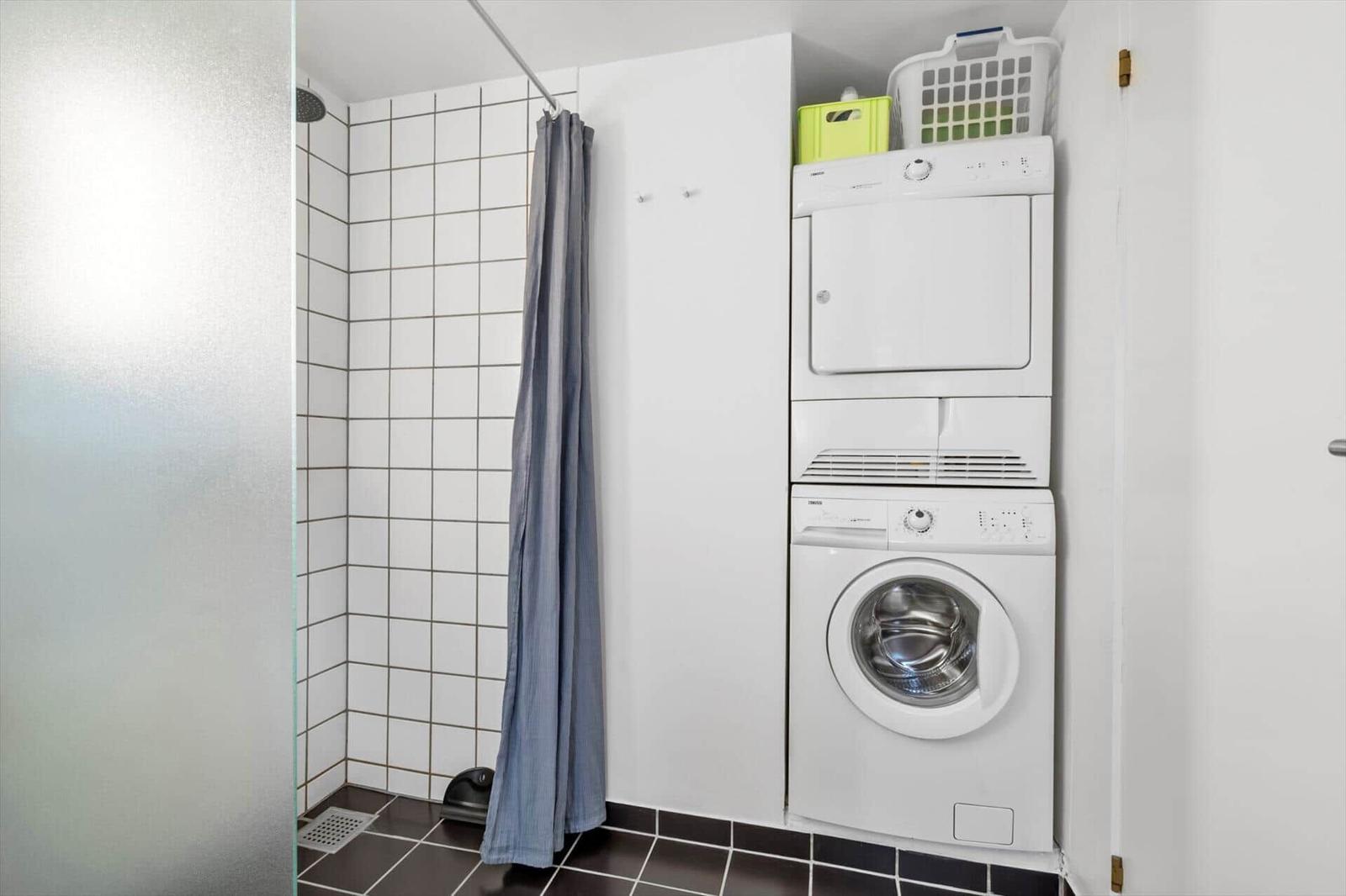 Shower with curtain and stacked washer-dryer unit against white wall.