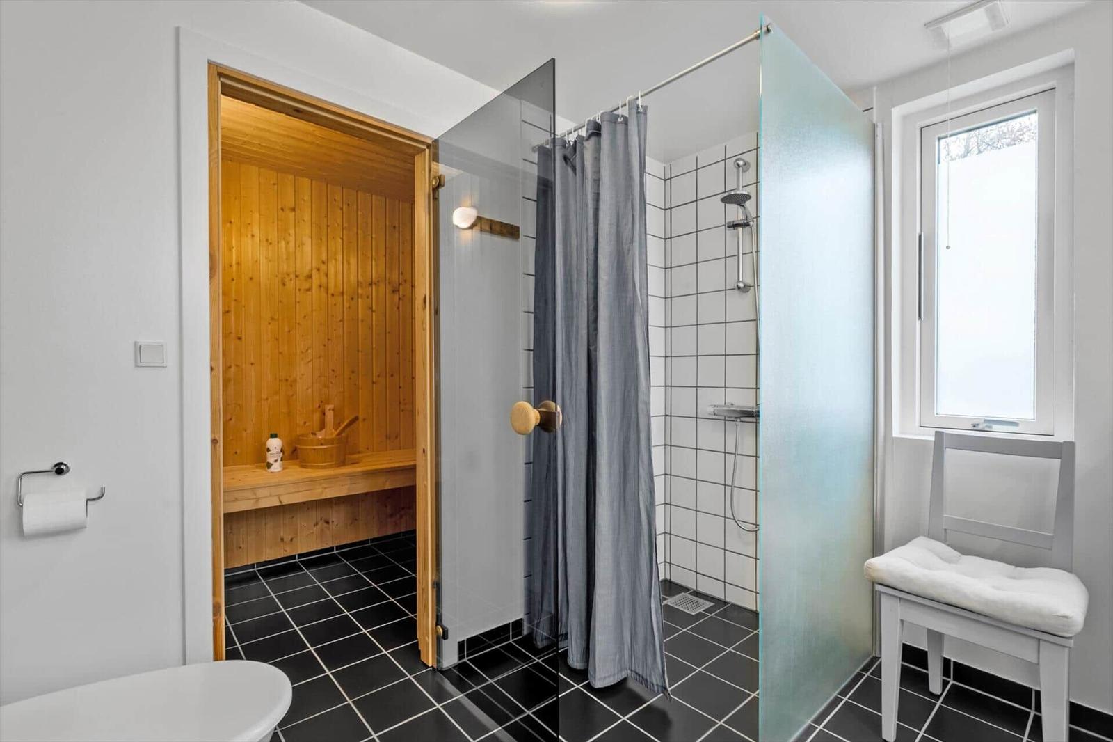 Bathroom with shower, sauna, and window with chair.