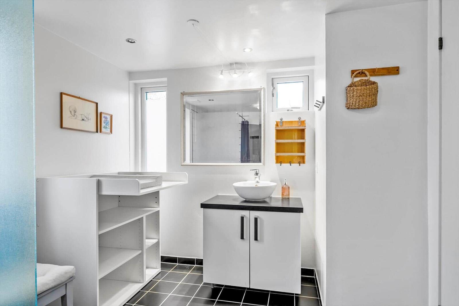 Bathroom with sink, mirror, and changing table. Black tiles and white walls.