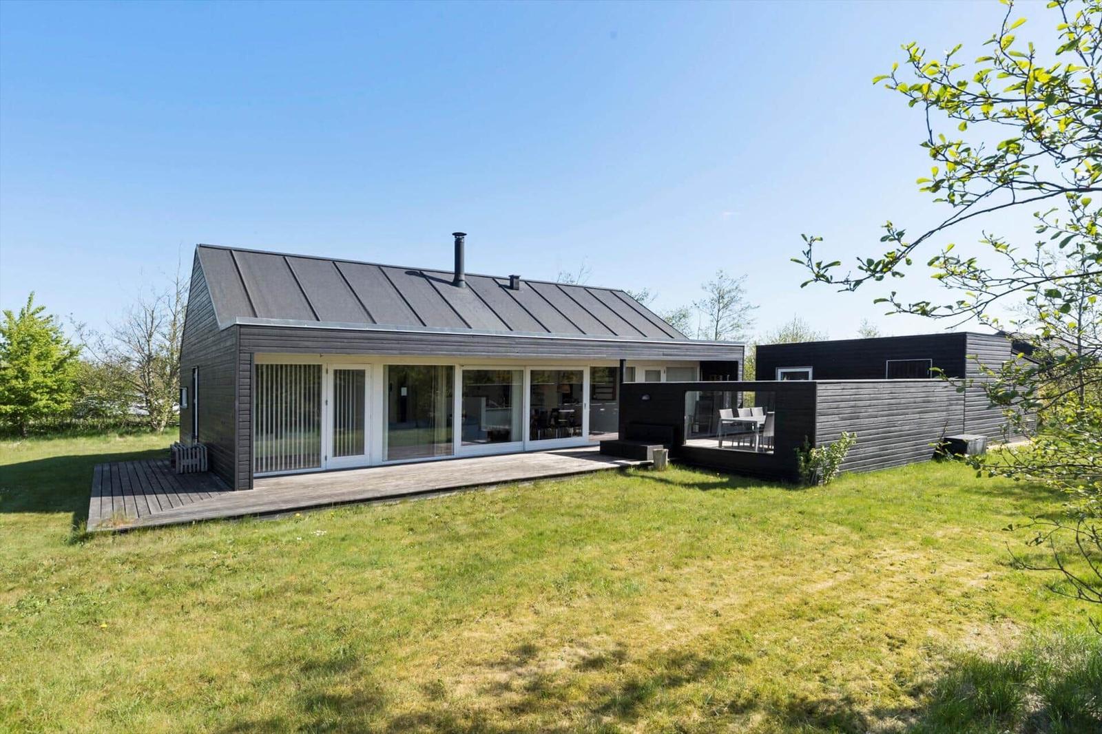 Modern wooden cabin with terrace and garden. Large glass front. Outdoor table with chairs.