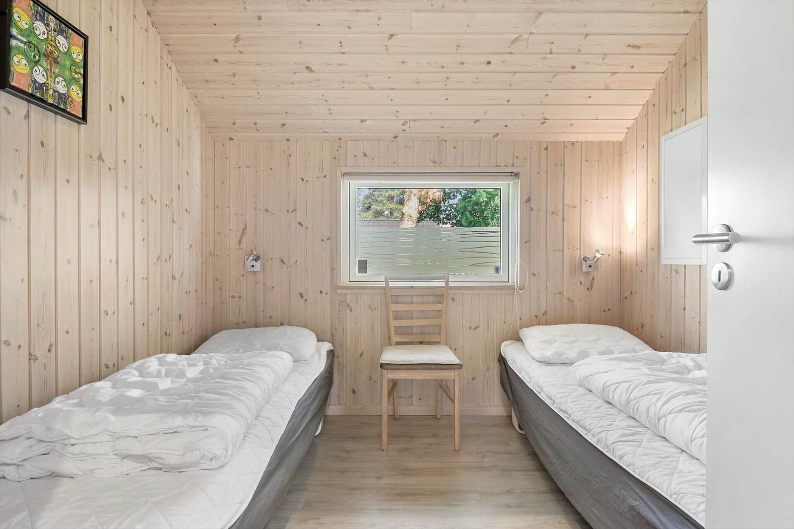 Two beds, chair, and window in a wood-paneled room.