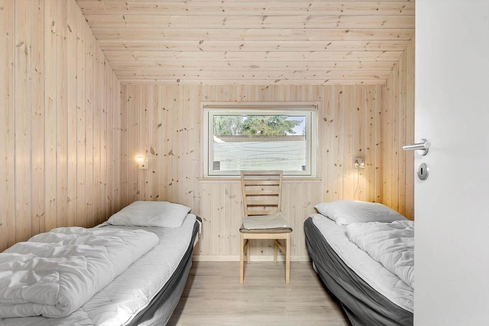 Two single beds, wooden walls, chair and window with view outside.