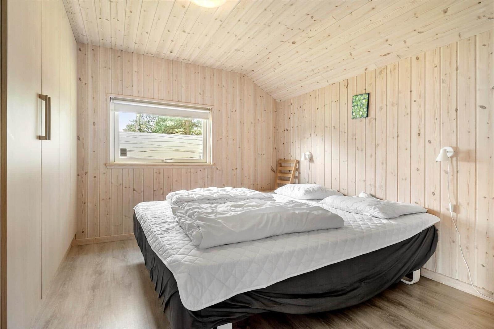 Bedroom with wooden paneling, bed, and window.