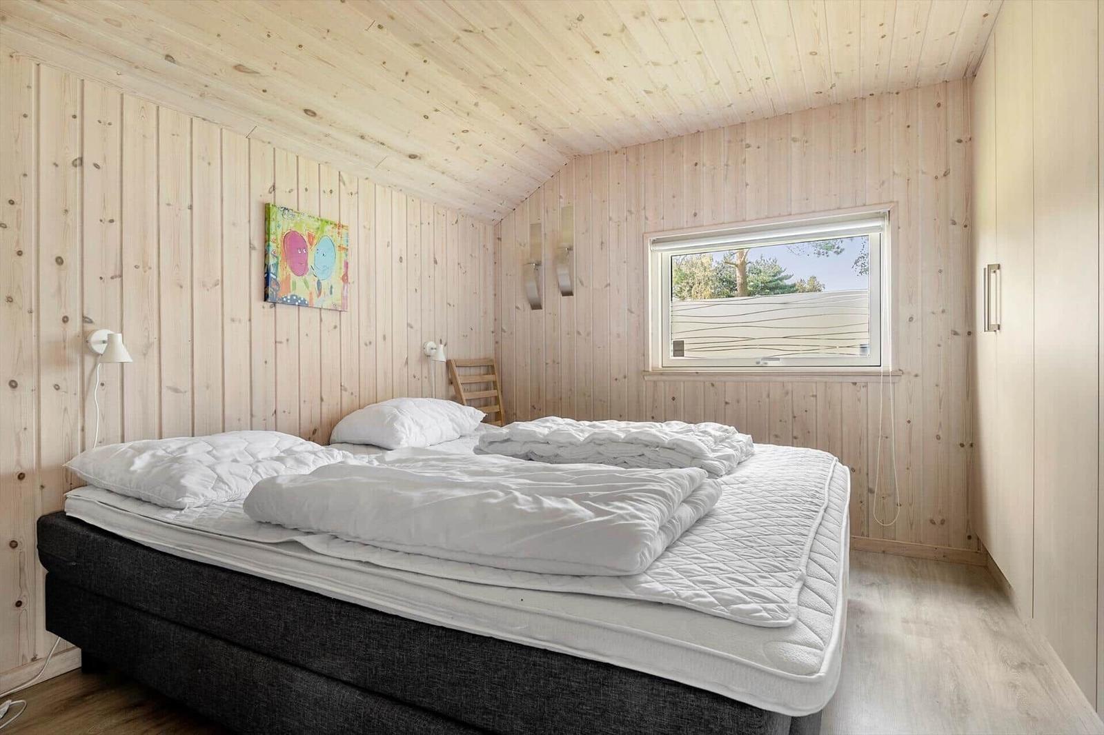 Bedroom with wooden walls, bed, and window with view outside.