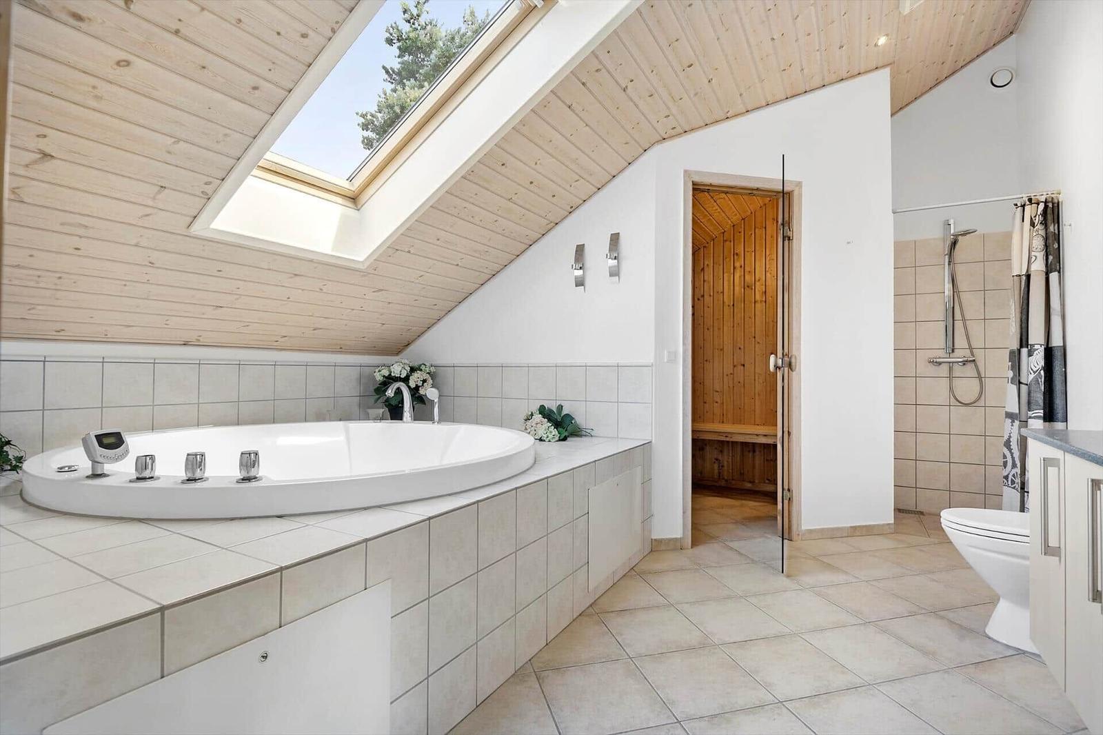 Bath with whirlpool, sauna, and shower under wooden ceiling with skylight.