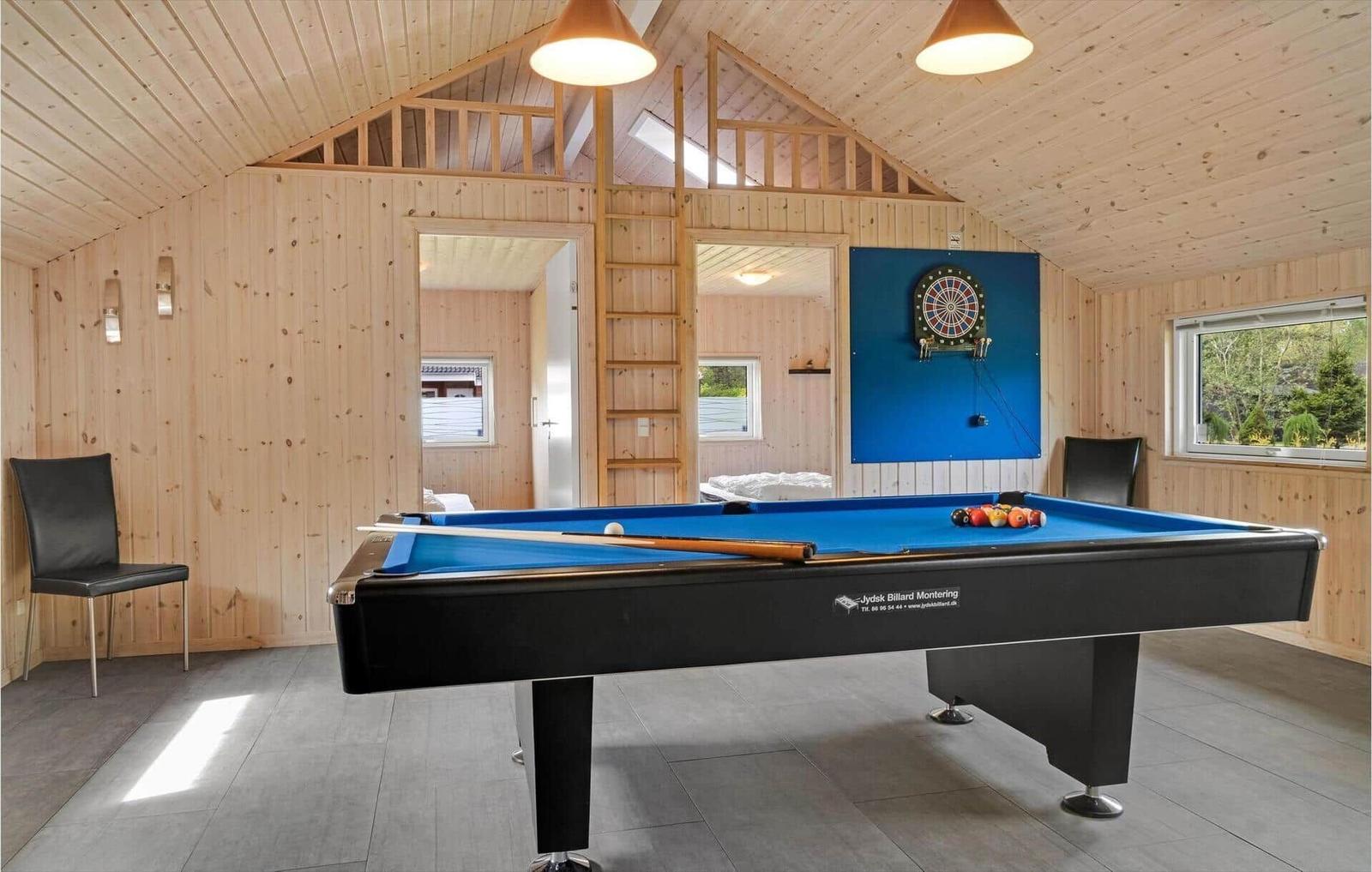 Room with pool table, dartboard, and wooden paneling. Loft with ladder.